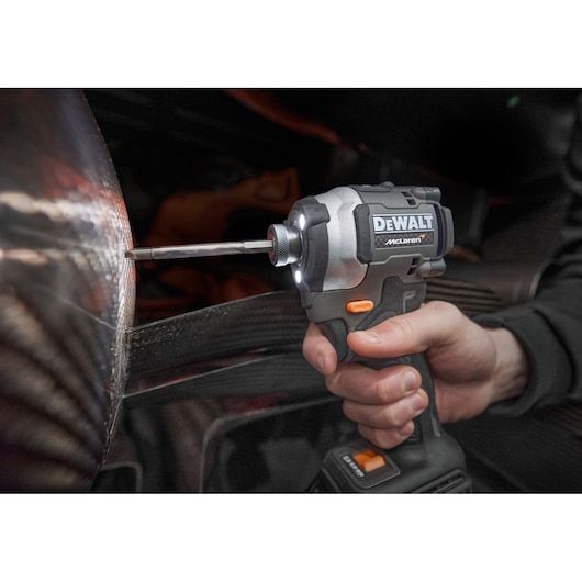 A close-up of a hand using a DEWALT McLaren cordless power tool, driving a screw into a metallic surface.