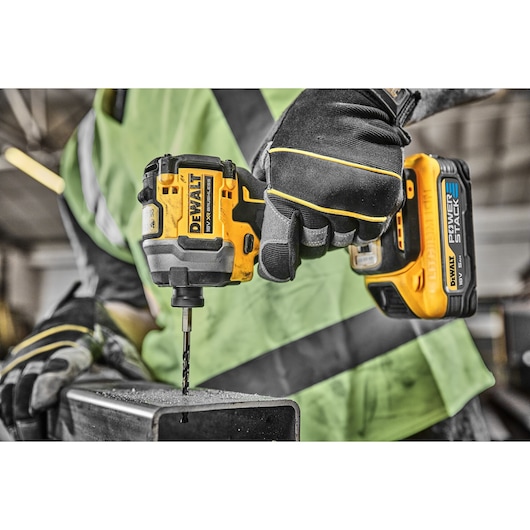 A close-up of a worker using a DEWALT cordless power drill with a POWERSTACK battery, drilling into a metal surface. The