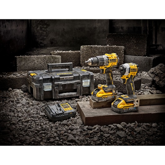 DEWALT toolset with two power tools, charger, and carrying case on construction site with concrete blocks.