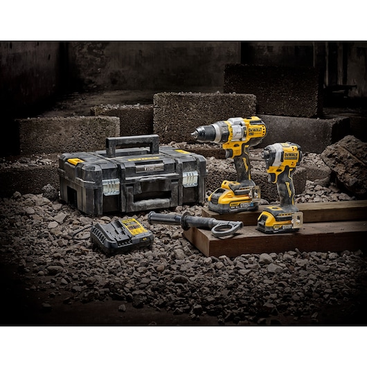 DEWALT tool kit with two drills, batteries, charger, handle, and case on a rocky construction site.