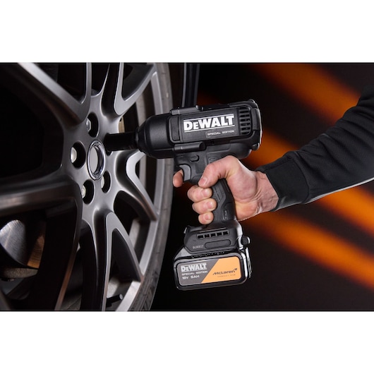 A person uses a DEWALT special edition cordless impact wrench to tighten or loosen a wheel nut on a car alloy wheel. The