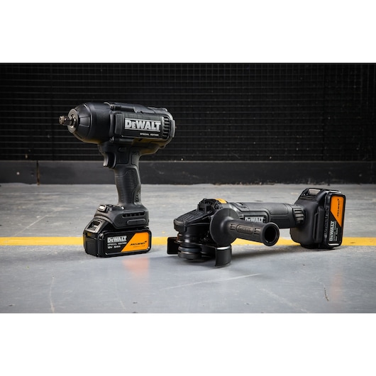 Two DEWALT cordless power tools, an impact wrench and an angle grinder, are shown on a workshop floor.