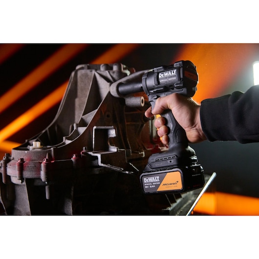 A close-up of a hand using a DEWALT cordless power tool next to a large metal machine part with orange light streaks in the