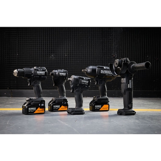 Four DEWALT power tools with batteries lined up on a concrete floor, photographed against a dark industrial background.