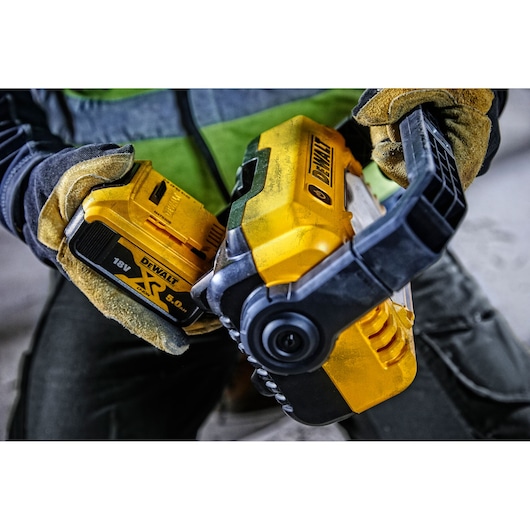 Gloved hands insert DEWALT 18V battery into yellow DCL077 LED work light for photography use.