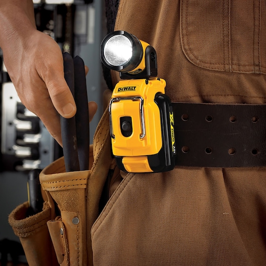 A DEWALT DCL510N compact yellow LED work light clipped onto a tool belt worn by a person dressed in brown workwear. The