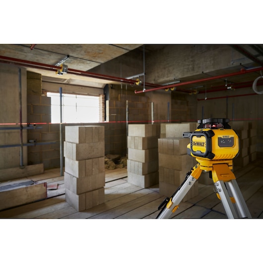 A DEWALT DCLE05211R laser level device mounted on a tripod is positioned in a construction site with concrete blocks