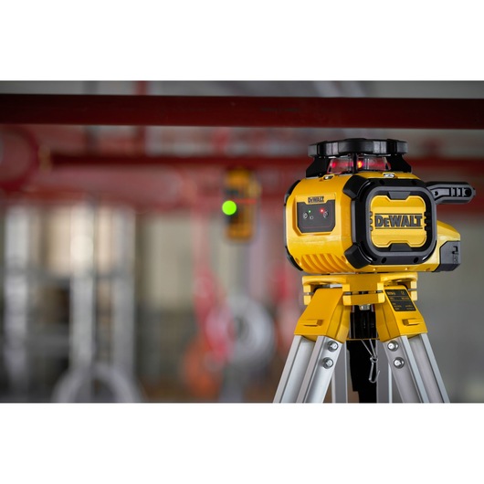 A DEWALT yellow rotary laser level (model DCLE05211R) mounted on a tripod in an indoor construction environment. The laser