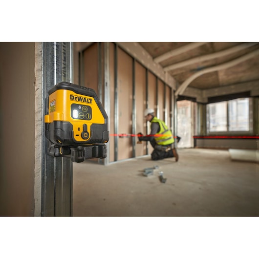 A DEWALT laser level device mounted on a metal beam in an unfinished building interior, projecting a red laser line across