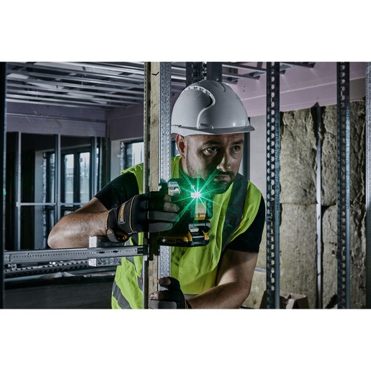 A construction worker wearing a hard hat and safety vest uses a DEWALT green laser level to align a metal frame inside a