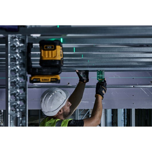 A construction worker wearing a hard hat and gloves is using a DEWALT tool to align metal beams. The worker is holding a