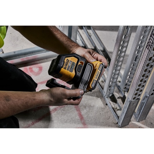 Person holding a DEWALT laser level tool near metal framing on a construction site floor.