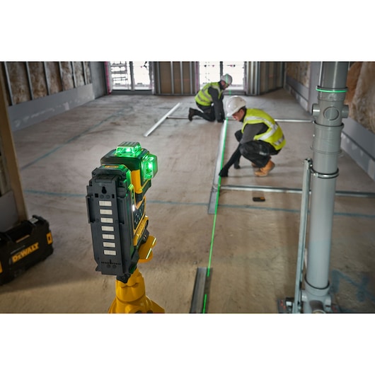 DEWALT green laser level tool on a tripod projecting lines for alignment in a construction site, with two workers in safety