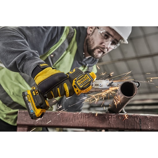 A person wearing protective gloves uses a DEWALT cordless tool to cut through a metal pipe, producing sparks.