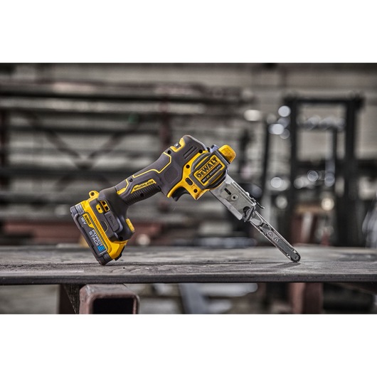 A DEWALT DCM200E2T cordless electric chainsaw with yellow and black design is placed on a metal surface in an industrial workshop setting.