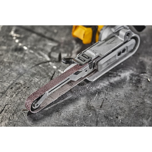 Close-up view of a DEWALT electric narrow belt sander resting on a scratched metal surface.