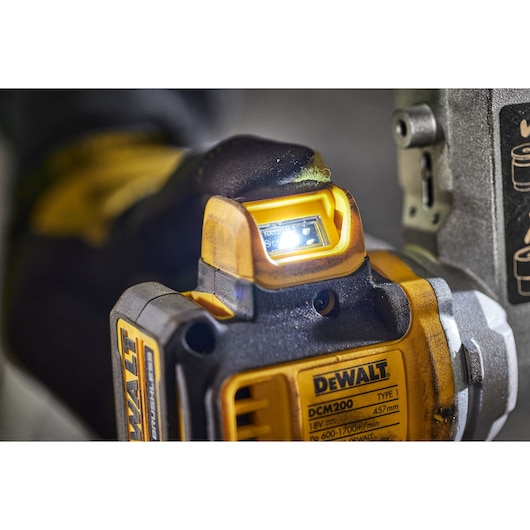 Close-up view of a DEWALT DCM200 power tool, showing the illuminated LED light and details on the tool's body, with a gloved hand holding it.
