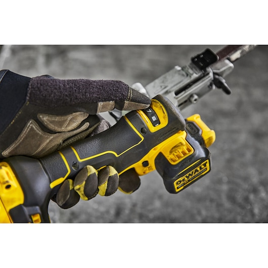 A close-up of a gloved hand operating a DEWALT cordless power tool, with the focus on the tool's handle and control buttons.