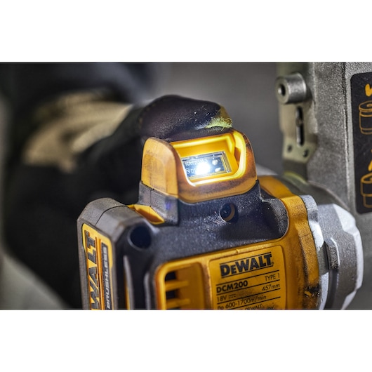 Close-up view of a DEWALT DCM200 power tool being used, with a bright LED light illuminated on the device.