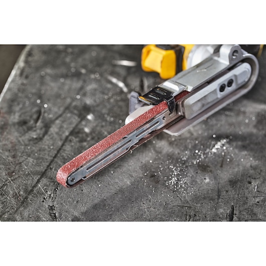 Close-up of a DEWALT DCM200N cordless file sander with a red sanding belt, placed on a metal work surface.