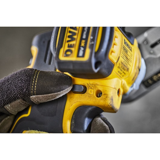 Close-up of a gloved hand pressing a button on a DEWALT DCM200N power tool, emphasizing the ergonomic design and control features.