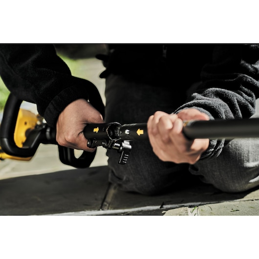 Close-up of a person assembling a DEWALT power tool by connecting two black metal rods with yellow arrows, outdoors on a stone surface.