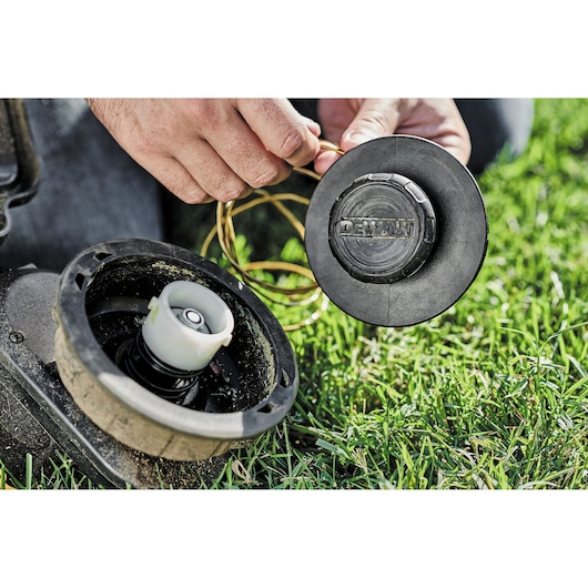 Close-up of a person holding and assembling the spool and line of a DEWALT string trimmer on green grass.