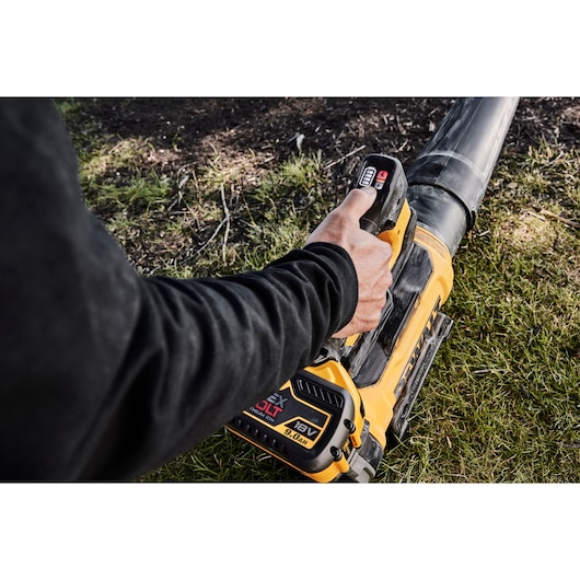 Hand holding a DEWALT 18V battery-powered blower, used on grass outdoors.
