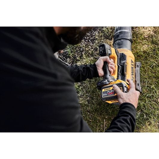Person using a DEWALT 54V FLEXVOLT cordless blower outdoors on grass.