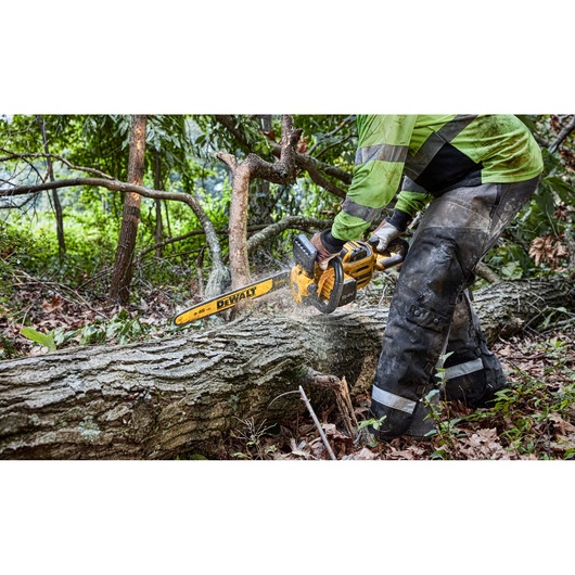 A person using a DEWALT cordless chainsaw to cut a fallen tree trunk outdoors in a forested area.