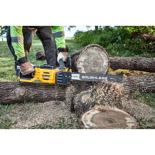A person wearing protective gloves and clothing uses a yellow DEWALT cordless brushless chainsaw to cut through a thick log
