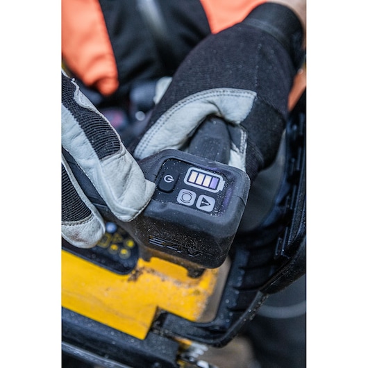 Gloved hand presses control buttons on a yellow DEWALT tool with battery level indicator visible.