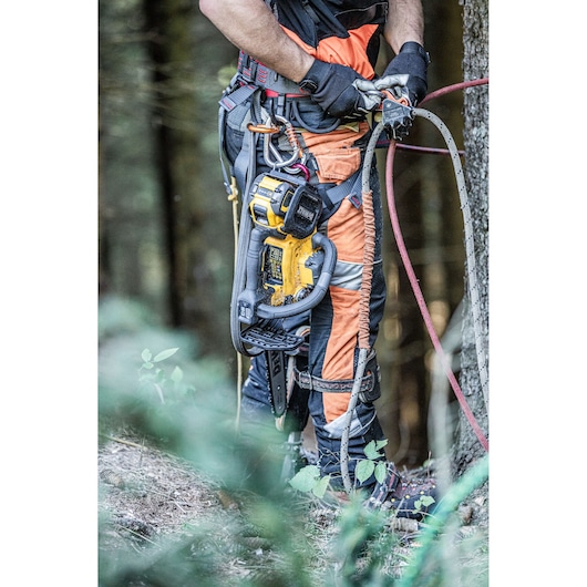 Worker in protective gear using DEWALT chainsaw and climbing equipment in a forest setting.