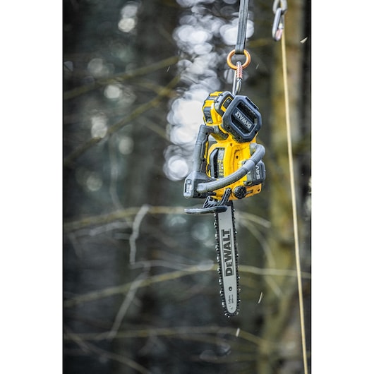 DEWALT battery chainsaw hanging by a rope outdoors in a forest setting.