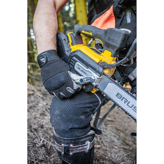Person wearing gloves adjusts a yellow DEWALT cordless chainsaw outdoors.