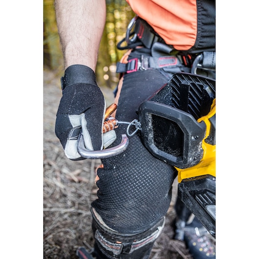Gloved hand clips a tool to a belt with a carabiner. DEWALT equipment is visible on the worker's leg.