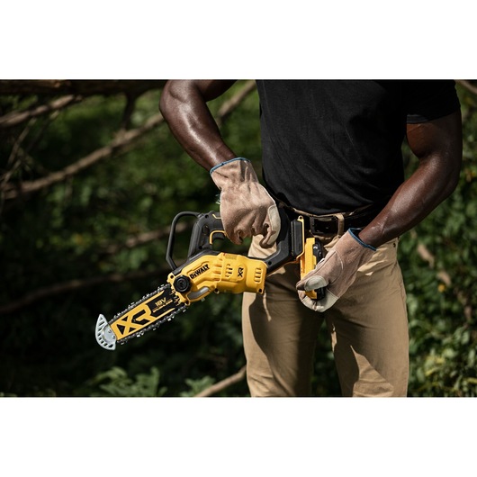 Person wearing gloves holding a DEWALT cordless chainsaw outdoors, preparing it for use.