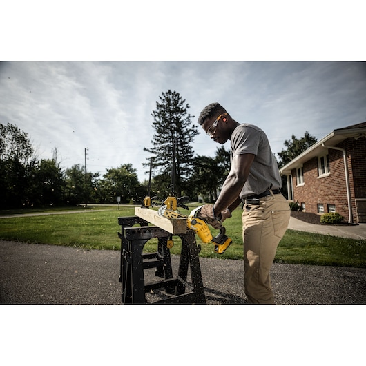 Person sawing wood outdoors using a DEWALT cordless chainsaw, with sawdust flying around.