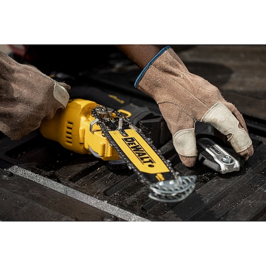 Gloved hands adjusting a DEWALT chainsaw on a black surface, focusing on the blade and tool.