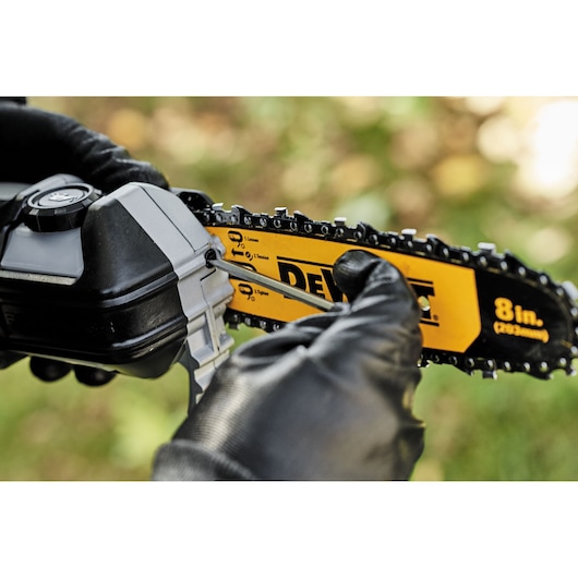 Close-up of a gloved hand adjusting the chain tension of a DEWALT 8-inch chainsaw bar using a tool.