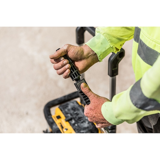 Close-up of a person wearing a yellow high-visibility work shirt adjusting the handle of a DEWALT portable device.