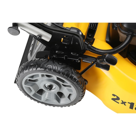 Close-up view of a DEWALT lawn mower wheel and height adjustment mechanism, showing part of the yellow mower body with '2x18' marking.