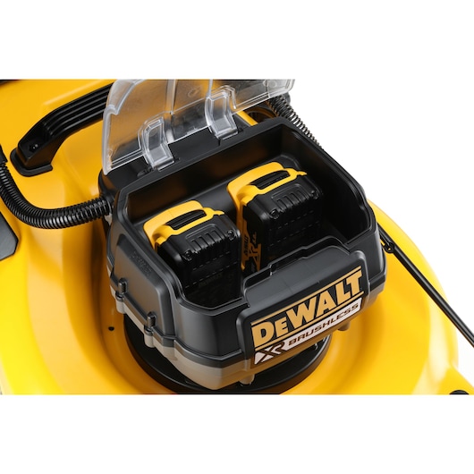 Close-up of DEWALT lawn mower battery compartment with two mounted batteries and transparent cover.