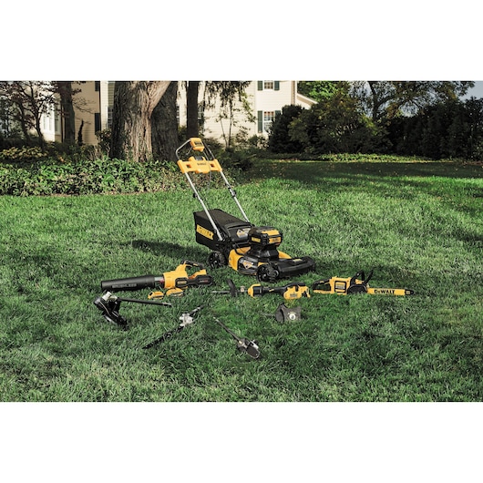 A set of DEWALT outdoor power tools, including a lawn mower, leaf blower, chainsaw, and several attachments, displayed on a green lawn in front of a house.