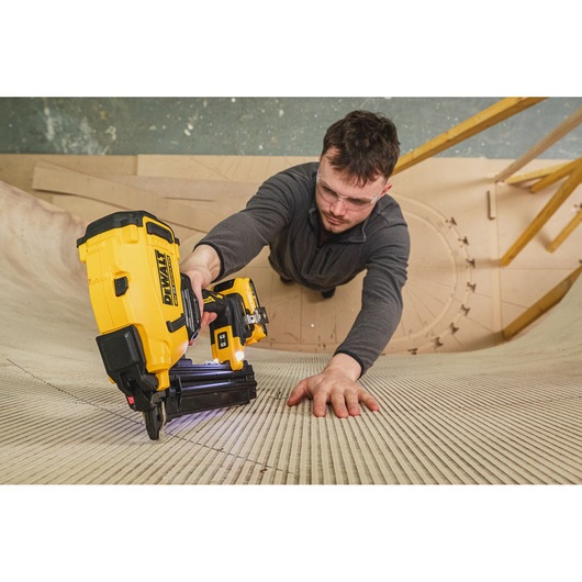 Person using DEWALT nailer DCN210SN-XJ on a curved wooden surface while wearing safety glasses.