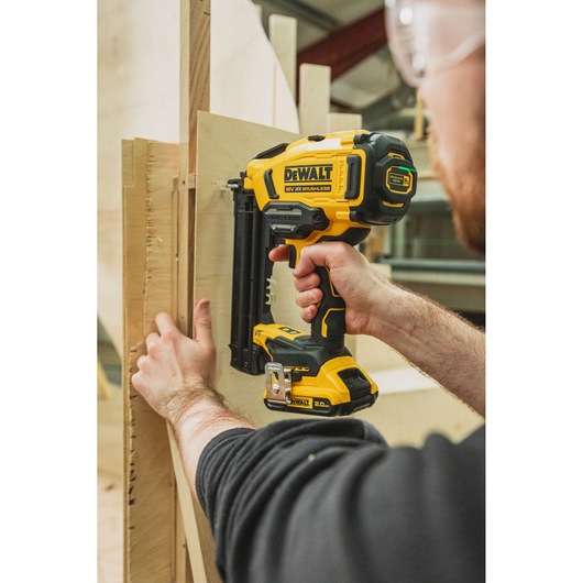Person uses DEWALT cordless nail gun to attach wooden boards in a workshop setting.