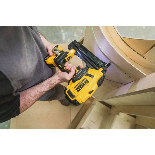 Person using a DEWALT cordless nailer to fasten curved wooden panels on a construction project.