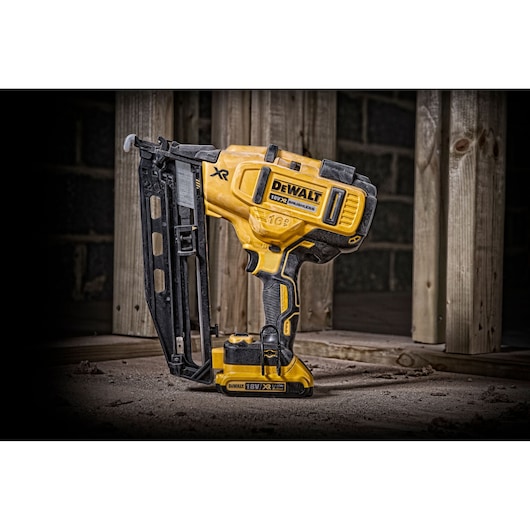 Yellow DEWALT cordless nail gun standing on a dusty floor near wooden framing.