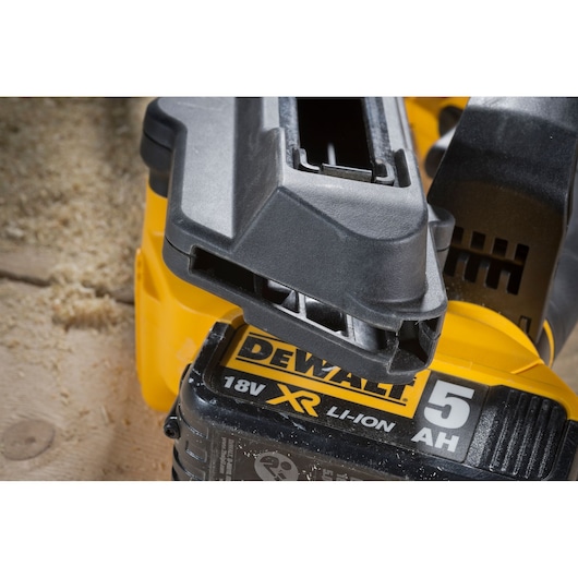 Close-up of a DEWALT 18V XR Li-Ion battery with 5Ah capacity attached to a yellow DEWALT power tool, with sawdust visible in the background.