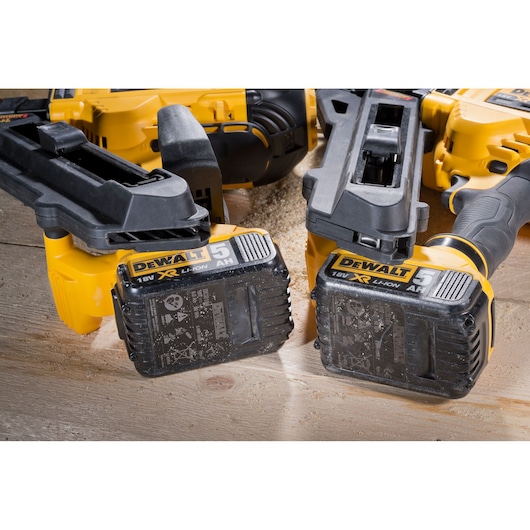 Close-up view of two DEWALT 18V XR Li-Ion 5Ah batteries attached to yellow power tools, placed on a wooden surface with sawdust.